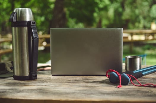 Laptop and Camping Gear on a Wooden Table Outdoors in a Natural Park Setting photo