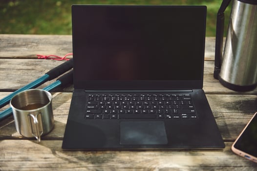 Laptop on Wooden Table Outdoors with Hiking Gear and Coffee photo