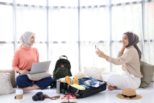 Two Young Asian Girls Prepare for Summer Trip, Book Tickets Using Laptop and Take Selfies for Today's Outfits photo