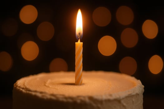 Close up of a single burning birthday candle on a frosted cake with soft warm bokeh lights photo