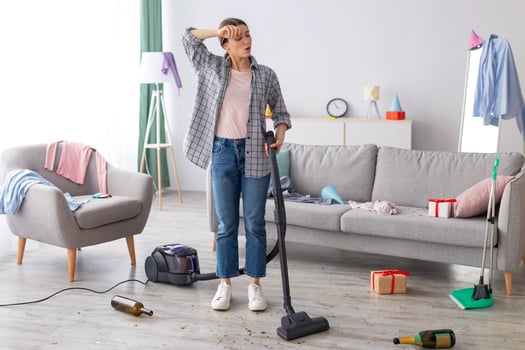 Tired young woman vacuuming her house after party, wiping her forehead, feeling tired of cleaning, free space. Exhausted millennial student getting rid of mess at university dorm room photo
