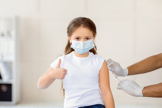 Successful coronavirus vaccination. Little girl showing thumb up gesture during covid-19 vaccine injection at hospital. Protection against virus and population immunization concept photo
