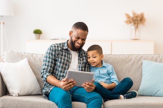 Black Dad And Son Using Digital Tablet Browsing Internet And Watching Cartoons Online Spending Time Together At Home. Weekend With Daddy. Family Gadgets Concept photo