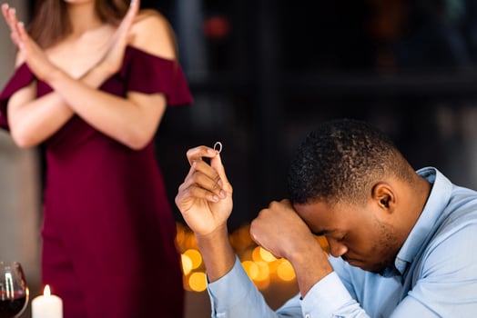She Said No. Woman Rejecting Marriage Proposal From Her Black Boyfriend, Upset African American Man Sitting At Table In Restaurant With Diamond Ring In Hand, Touching Head In Despair, Selective Focus photo