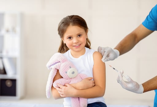 Happy little girl with toy bunny getting coronavirus vaccine injection at hospital. Black doctor immunizing child against covid-19 virus at clinic. Healthcare and medical concept photo