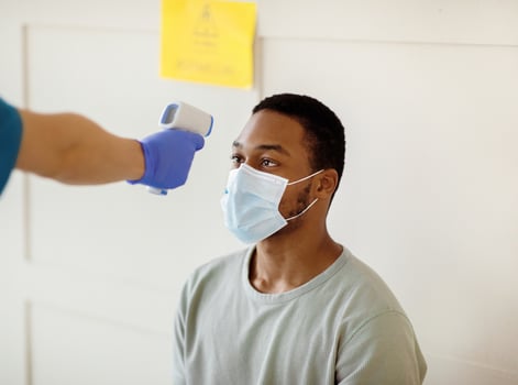Young black man having his temperature measured by infrared thermometer at clinic before getting covid-19 vaccine injection. Population immunization and health service concept photo