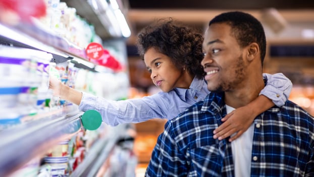 Happy black father with his cute daughter shopping for dairy products at big mall. Lovely girl with her dad purchasing groceries at supermarket, buying foodstuff together photo