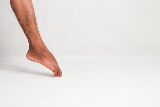 A bare male leg and foot of a black man touching the white floor in studio photo