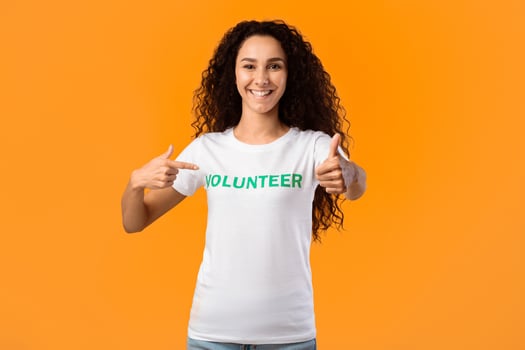Happy Female Volunteer Gesturing Thumbs-Up Pointing At Herself Posing Standing On Yellow Studio Background, Smiling To Camera. Female Activist Showing Like Approving Volunteering Work photo