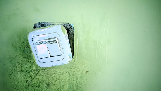 A white light switch is on a green wall photo