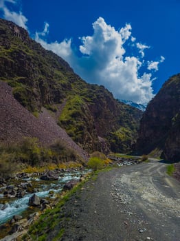 Majestic river flows peacefully through rocky Kyrgyzstan mountains under a clear blue sky. Dirt road meanders alongside, inviting adventurous exploration in nature's tranquility. photo
