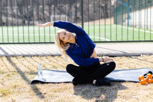 Young woman stretching on mat in a park during sunny day photo