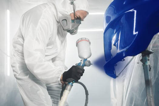 Professional bodywork, male car painter in protective mask and workwear apply few layer paint from spray gun to automobile body parts in garage booth. photo