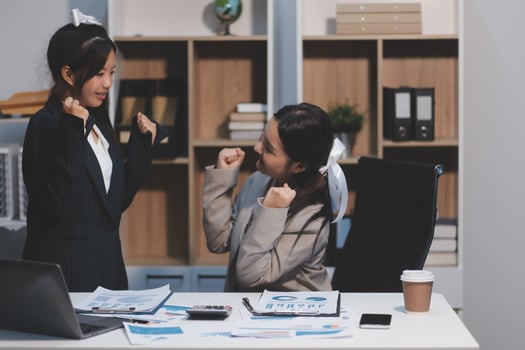 Two women in business attire are having a conversation at a desk photo