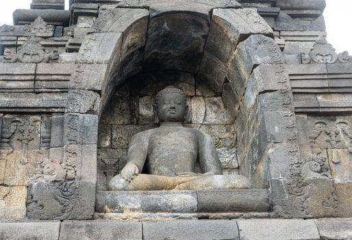 A Buddha statue sits calmly in a stone niche on Borobudur temple, surrounded by ancient carvings. photo