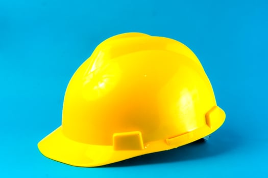 A bright yellow construction hard hat on a blue background. Safety helmet for industrial workers, engineers, and builders, symbolizing workplace protection and occupational safety. photo