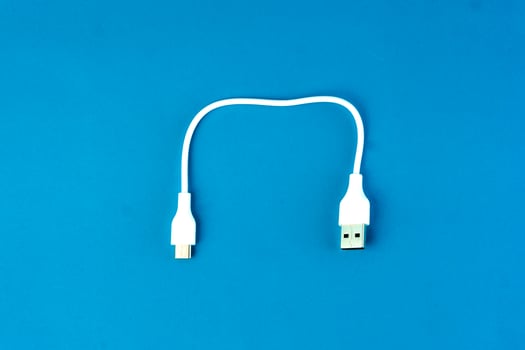 Short white USB to micro-USB cable on a blue background. Ideal for charging and data transfer for smartphones, tablets, and electronic devices. Compact and portable for everyday use. photo