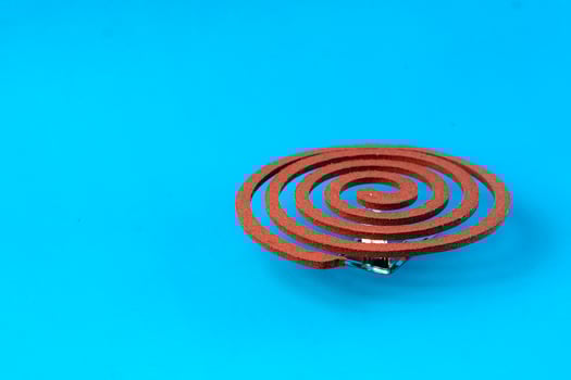 Mosquito coil placed on a metal stand against a blue background. Traditional insect repellent used to keep mosquitoes away, ideal for indoor and outdoor protection. photo