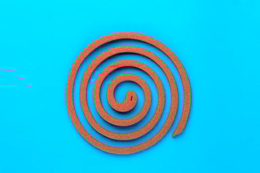 A single brown mosquito coil in a spiral shape on a blue background. Traditional insect repellent used for mosquito control, providing protection for indoor and outdoor environments. photo