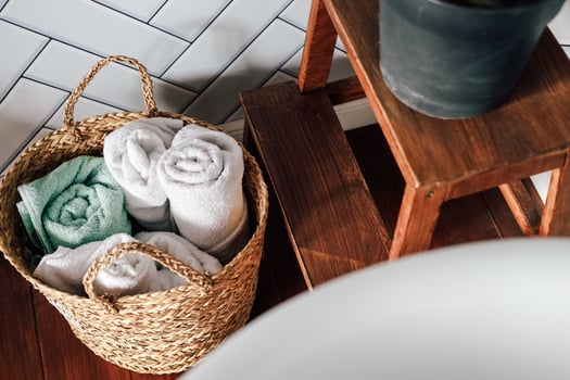 Cozy bathroom setting with rolled towels in a woven basket and wooden stool photo