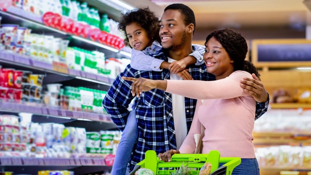 Family shopping. Young black parents with their cute daughter selecting food,pointing at shelves in supermarket. Joyful black girl with mother and father buying products at dairy department of store photo
