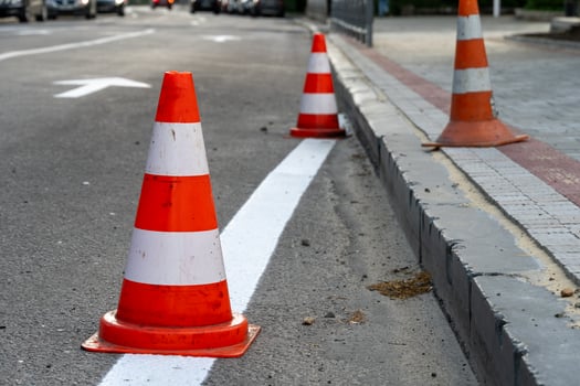 Traffic cones line the street, indicating ongoing construction work. Vehicles are rerouted while new boundaries are being established in an urban neighborhood photo