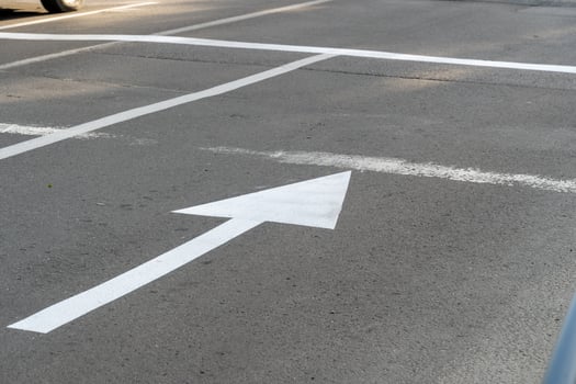 A clear view of white road markings on asphalt shows directional arrows and lines guiding vehicles. This image captures a well-maintained urban street scene photo