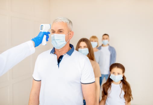 Medical doctor measuring senior man's temperature with electronic thermometer at hospital, free space. People waiting in line for covid -19 immunization. Vaccination against coronavirus concept photo