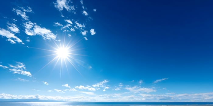 Bright Sun Shining Over Calm Ocean with Blue Sky and Clouds photo