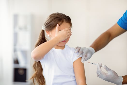 Scared little girl receiving covid-19 vaccine, covering her eyes in fear of injection at clinic. Cute child being immunized against coronavirus at hospital. Medical protection against virus concept photo