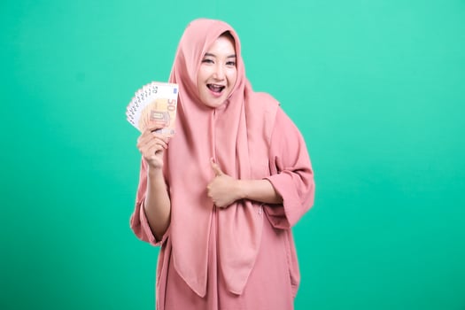 Cheerful Muslim woman holding euro bills giving thumbs up gestur photo