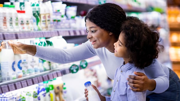 Positive black mom with her child shopping for products at dairy section of mall. Cheerful African American parent with her daughter buying groceries at huge hypermarket photo