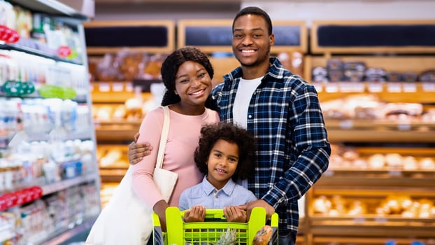 Portrait of smiling black parents with their daughter purchasing groceries at big supermarket. Millennial African American family shopping for products, buying food at hypermarket or mall photo