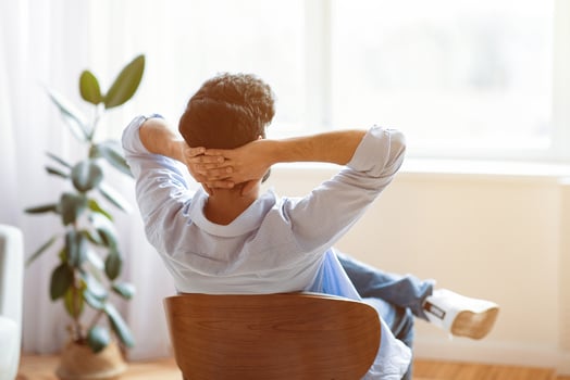 Rear view of unrecognizable man relaxing on chair in cozy interior at home with hands behind head, dark haired male leaning back and looking to window, enjoying lazy domestic day off, copy space photo