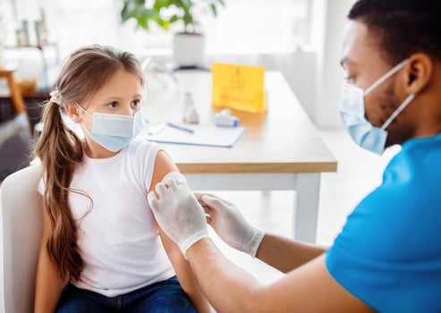 Male doctor or nurse giving shot of coronavirus vaccine to little patient's shoulder at clinic. Lovely girl being immunized against covid-19. Medical service and viral disease prevention concept photo