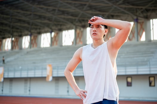 Asian man in white tank top standing with hand on waist and wiping sweat after running on racetrack. photo