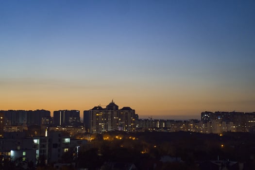 Urban skyline at dusk, showcasing illuminated buildings against a gradient sky transitioning from orange to deep blue, creating a serene evening atmosphere with city lights photo