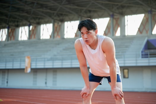 Asian man in white tank top standing with hands on his knee, taking a rest after running on racetrack. photo