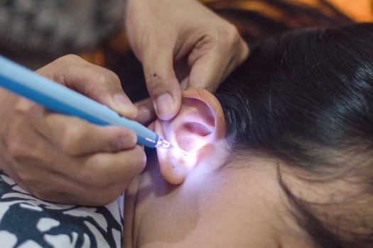 Woman cleaning her ears with an earwax cleaning stick equipped with flashlight. Self care at home. photo