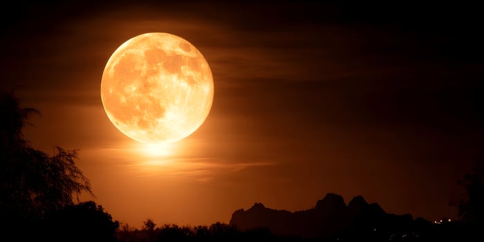 Large Orange Full Moon over Silhouetted Landscape at Night photo