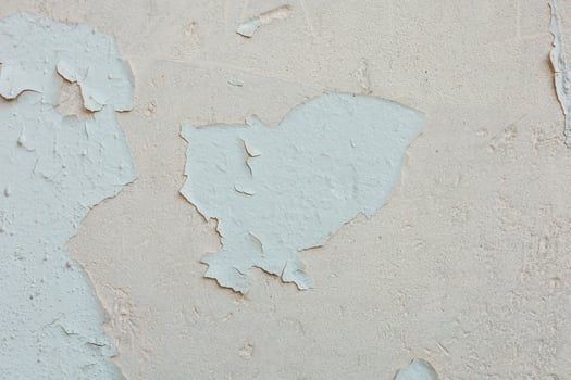 Cracked and peeling paint on a textured wall in a sunlit room revealing layers beneath photo