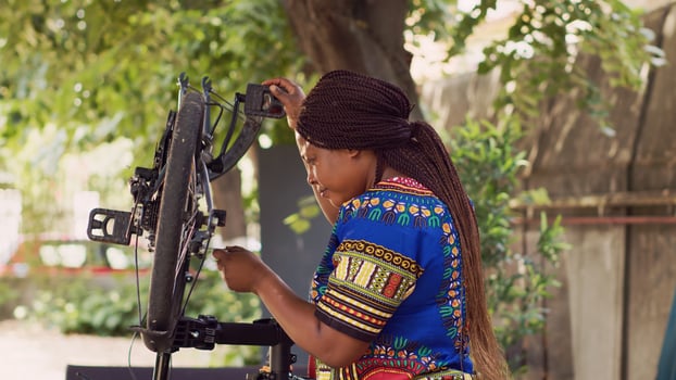 Determined female cyclist using specialized work tool to repair and adjust bike rear derailleur. Sporty african american woman mending her bicycle with professional multitool in home yard. photo