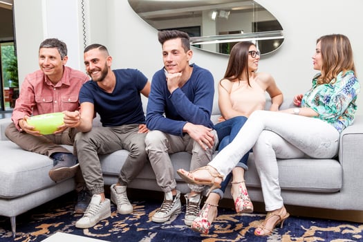 group of three friends and two girlfriends smiling having fun sitting on the sofa eating popcorn and watching tv photo