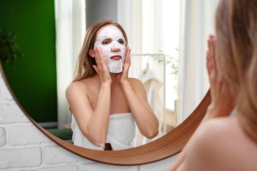 Woman applying a facial mask in the mirror during a self-care moment at home in natural light photo