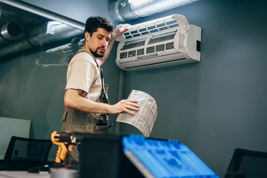 Technician performs air conditioner maintenance in modern office with blue walls and exposed ductwork photo