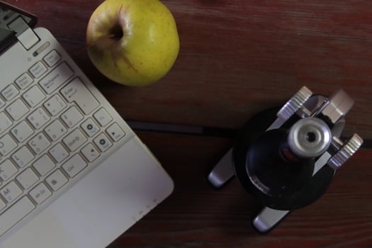 There is a microscope and a laptop on the wooden table. The emphasis is on the apple. photo