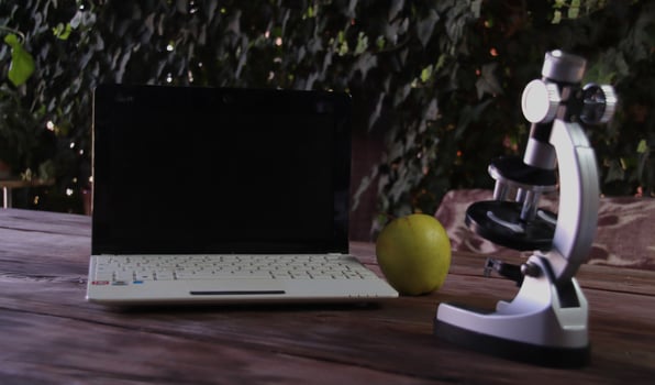There is a microscope, a laptop, and a green apple on a wooden table. Concept of learning and research photo