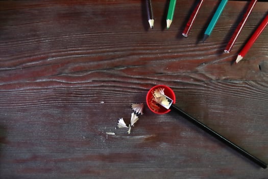 A red pencil sharpener and pencil shavings lie on a wooden table, top view. photo