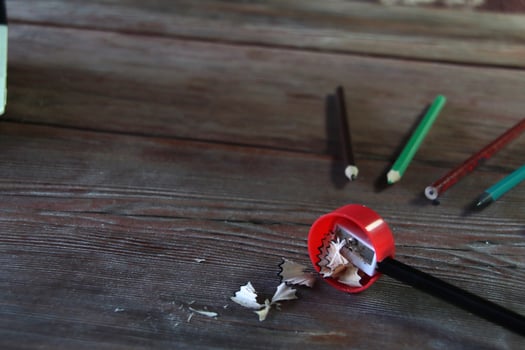 On a wooden table there is a red sharpener and pencil shavings photo