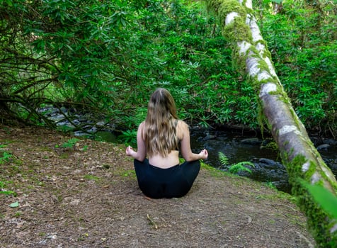 A woman sits in a lotus position in the woods by a river photo